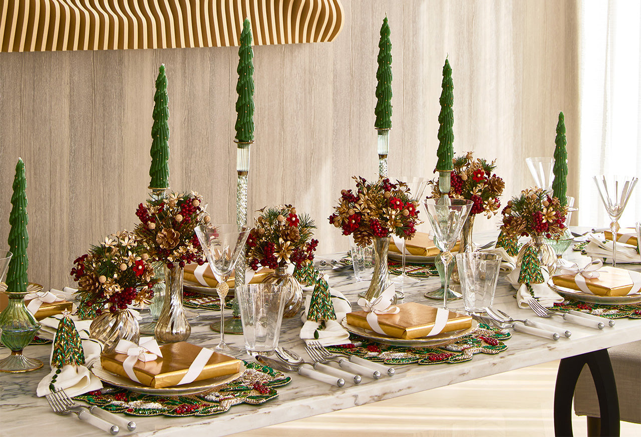 Red and gold Christmas tablescape with luxury placemats, evergreen centerpieces, and tree candles creating a festive holiday setting