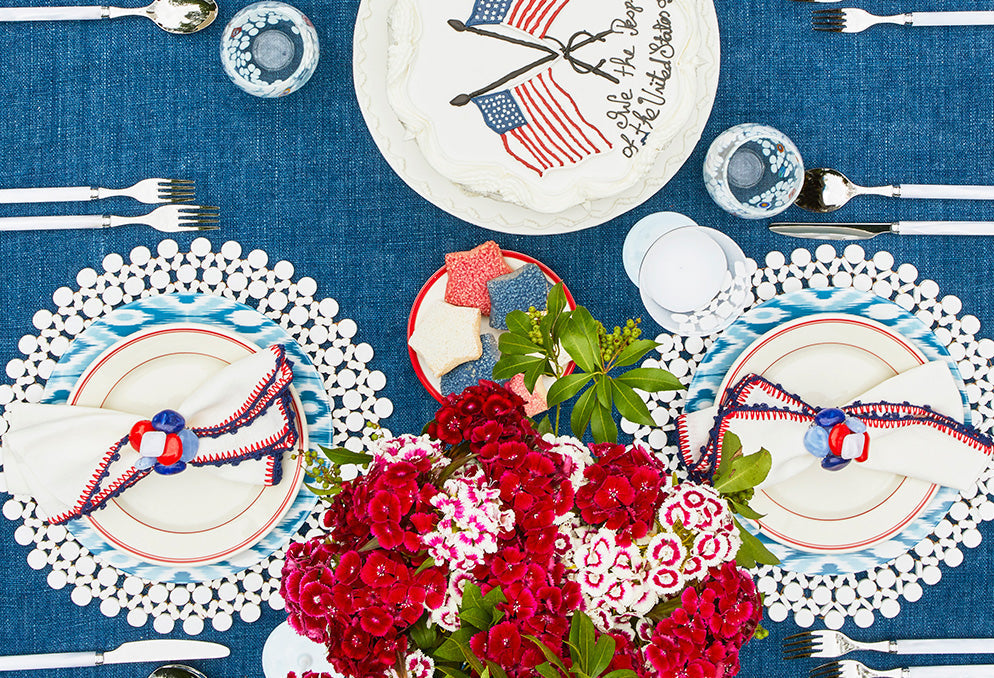 Fourth of July tableware setup in red, white, and blue with American flag decor and festive summer flowers on holiday table.