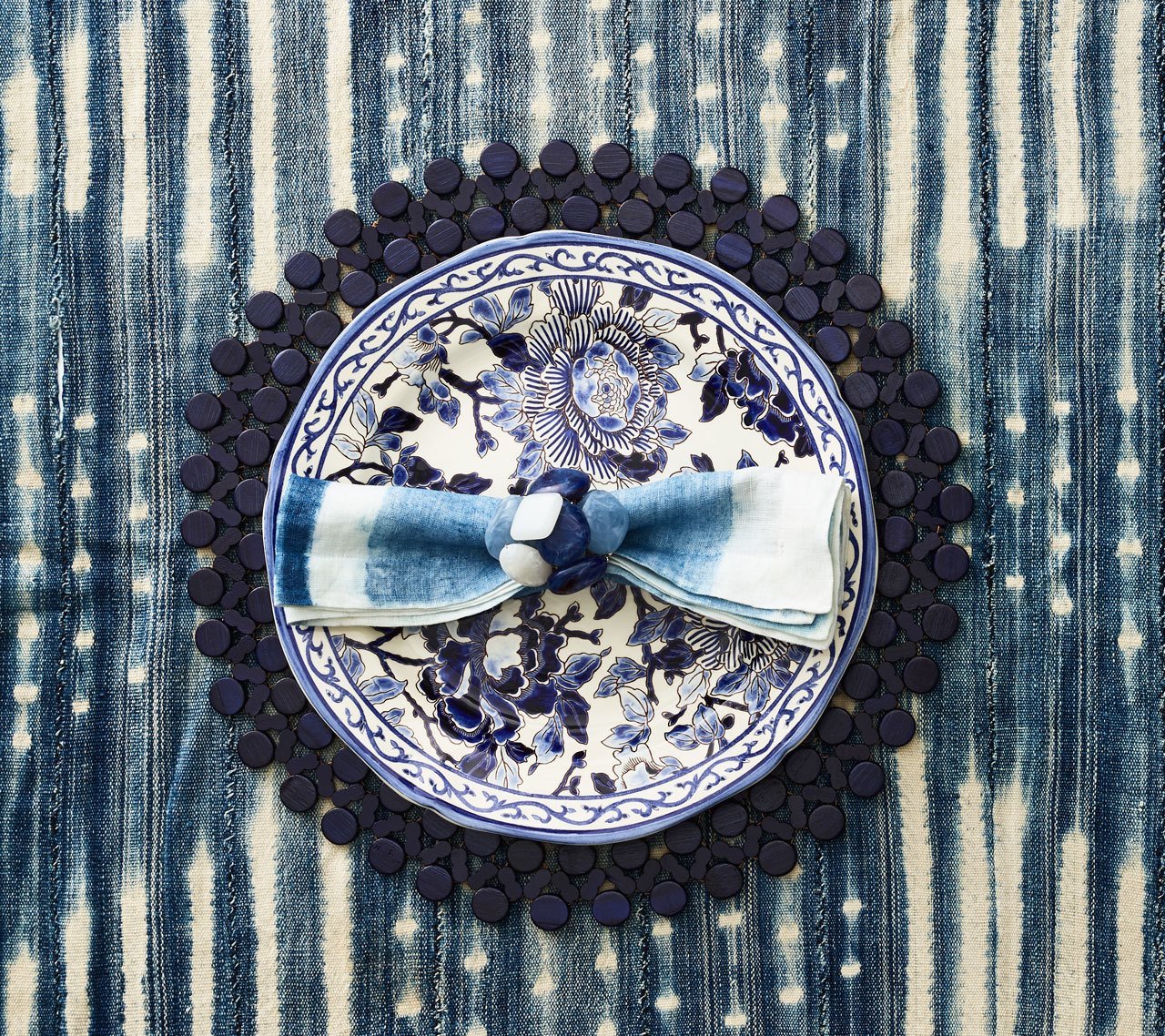 Round Bamboo Placemat in navy blue underneath a patterned plate and linen napkin of similar colors