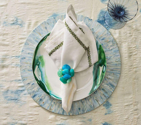 Tahiti Placemat in periwinkle on top of a white plate with green accents, a white napkin with green border, and a blue & green napkin ring
