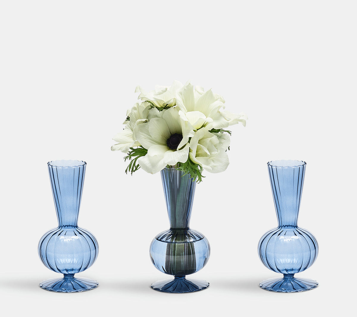 A glass Tess Bud Vase with white flowers in between two other Tess Bud Vases