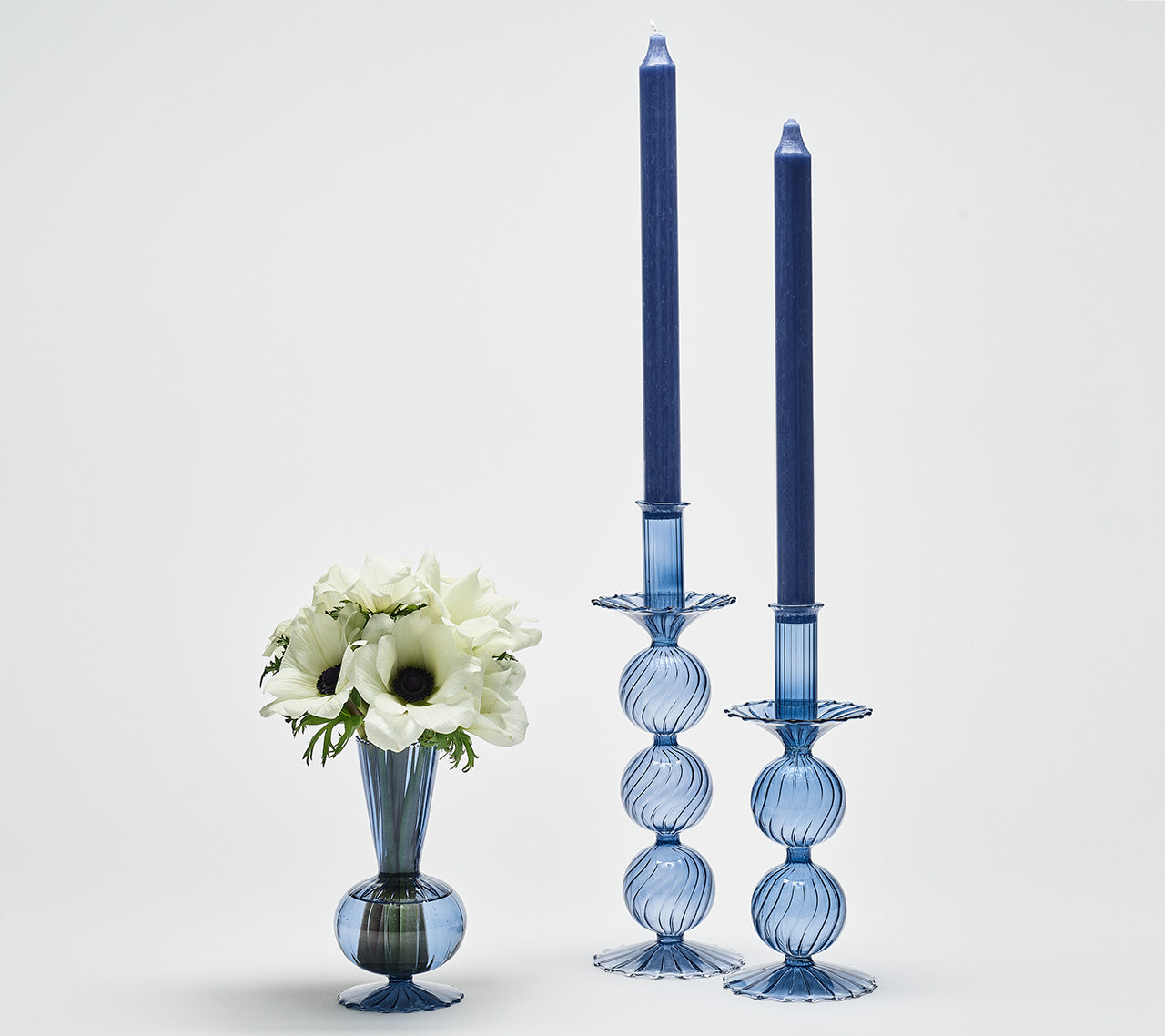 Two Iris Tall Candle Holder in cadet blue next to a blue vase with white flowers