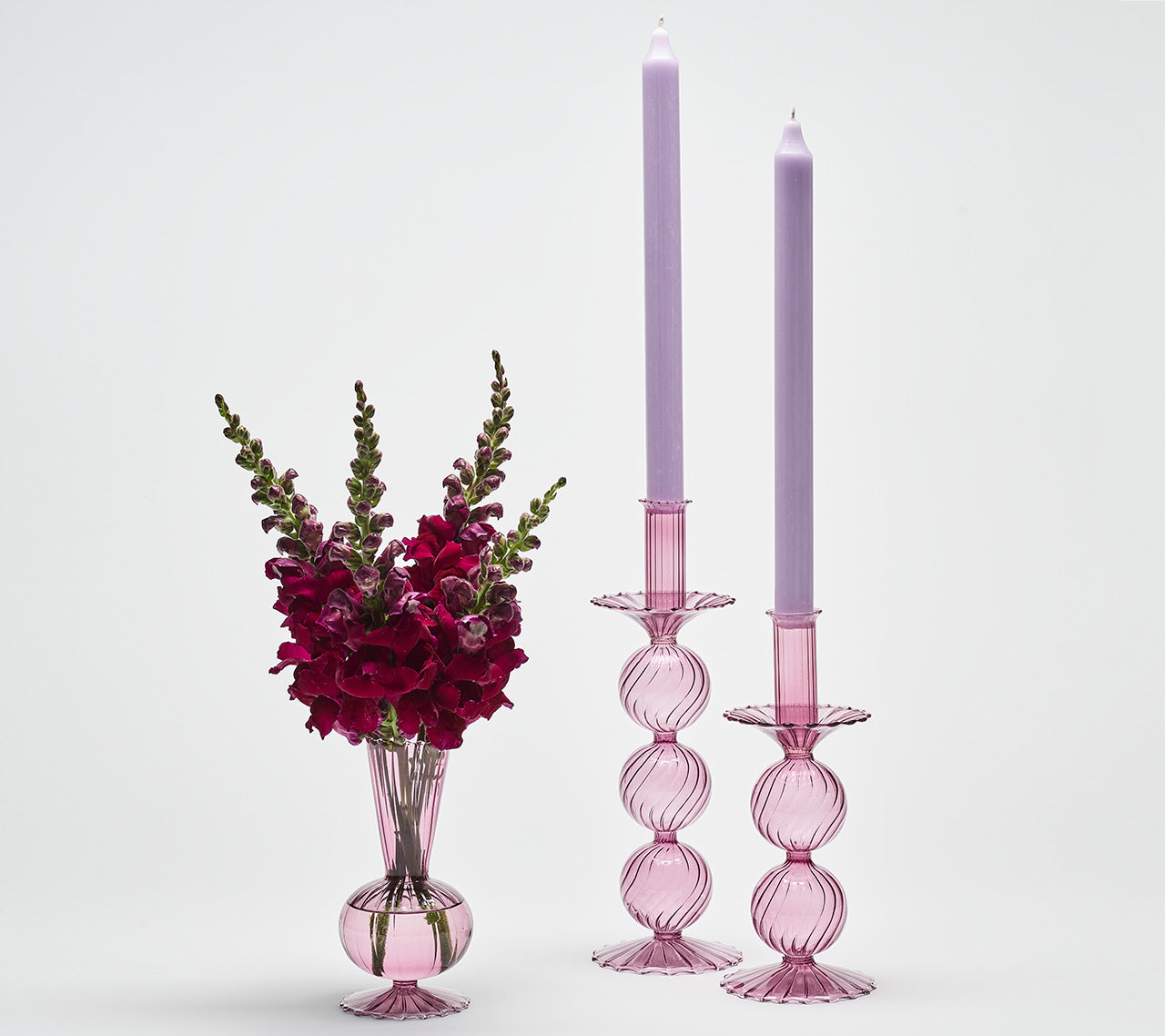 Two lavender glass Bella Short Candle Holders next to a vase with dark pink flowers