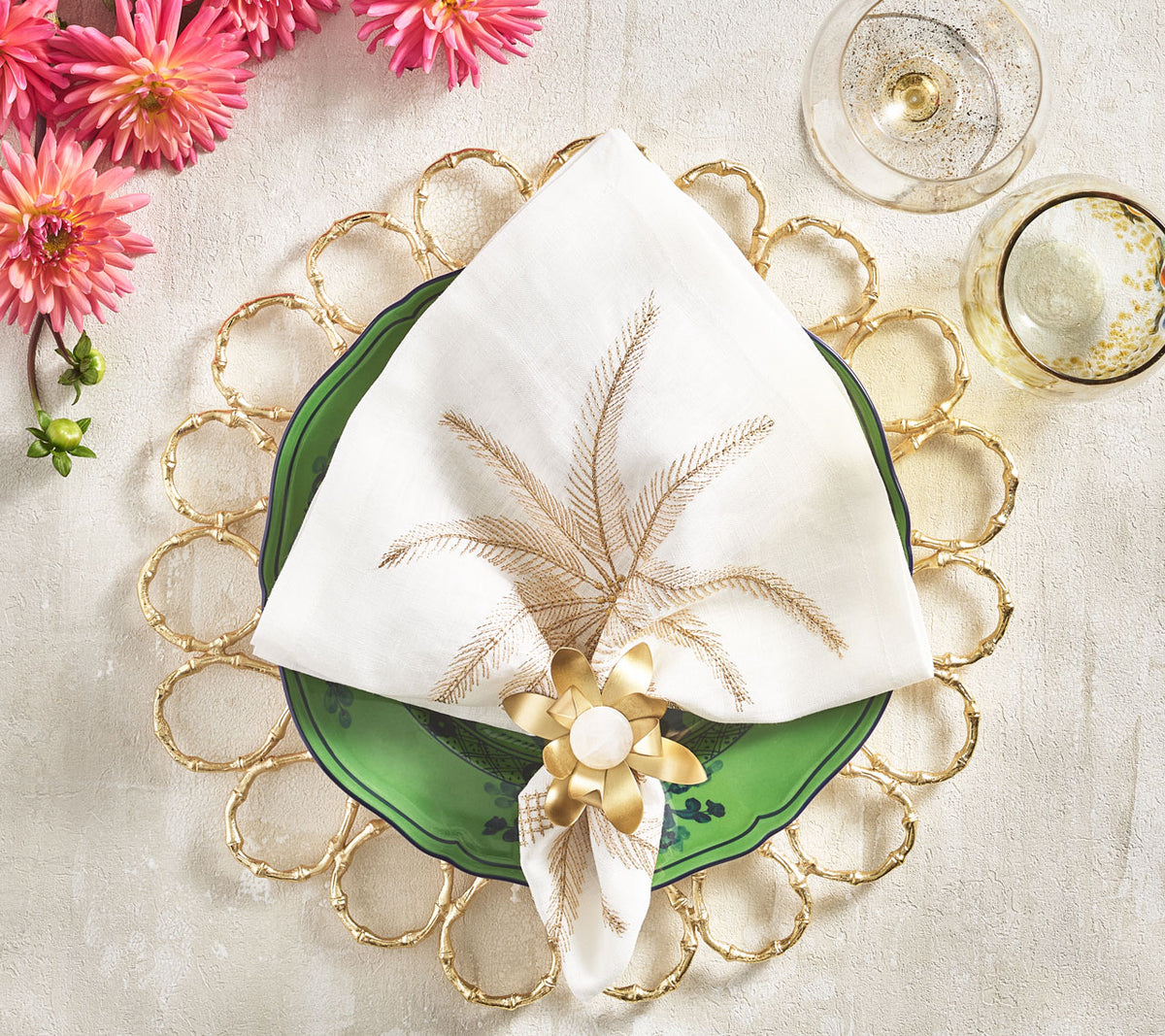 Place setting with a gold-ring placemat, green plate & a white Palm Coast Napkin with a natural and gold palm frond  