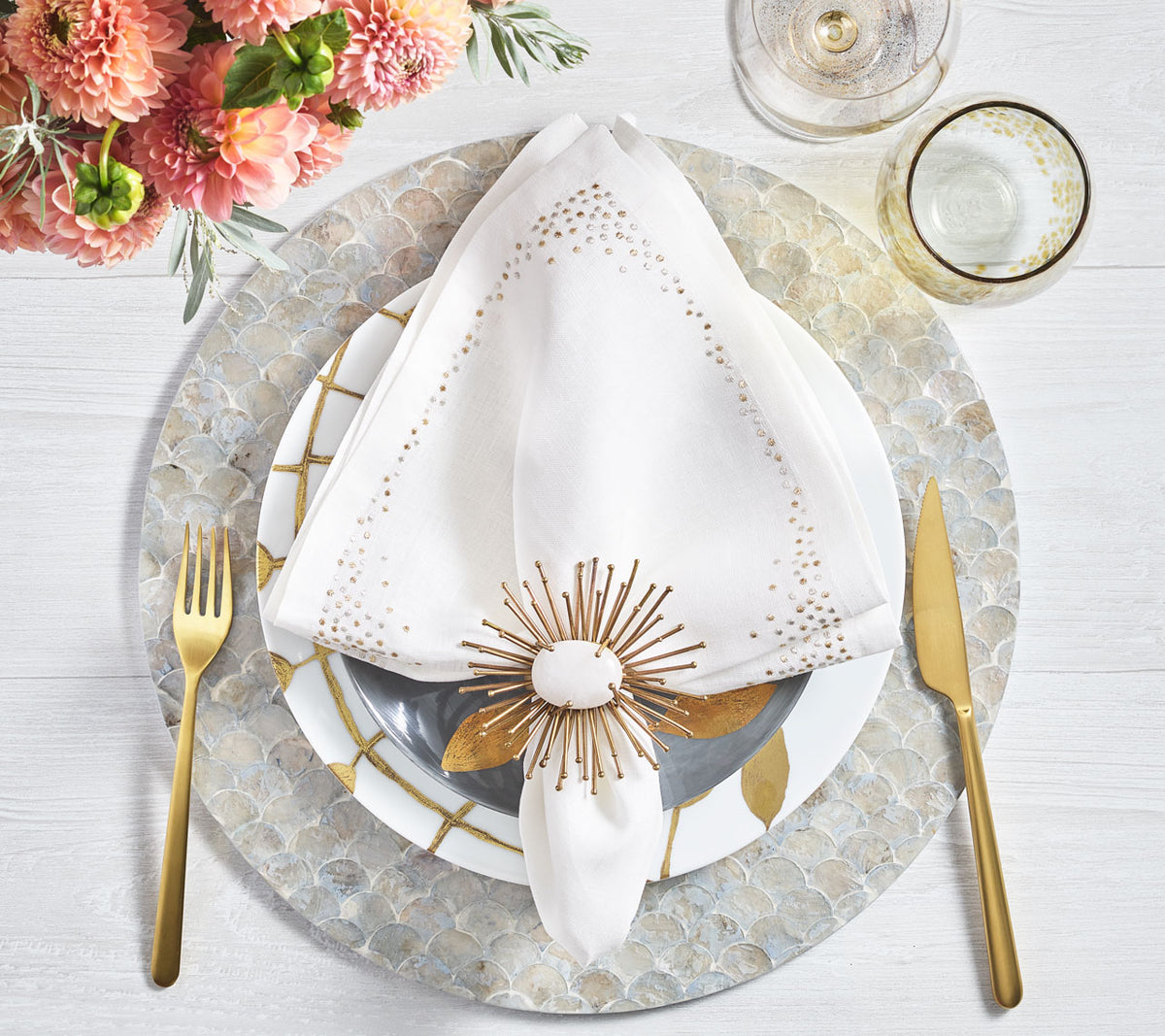 Place setting with gold accents like wine glasses, cutlery, a napkin ring and the white Pin Dot Napkin with its gold and silver border