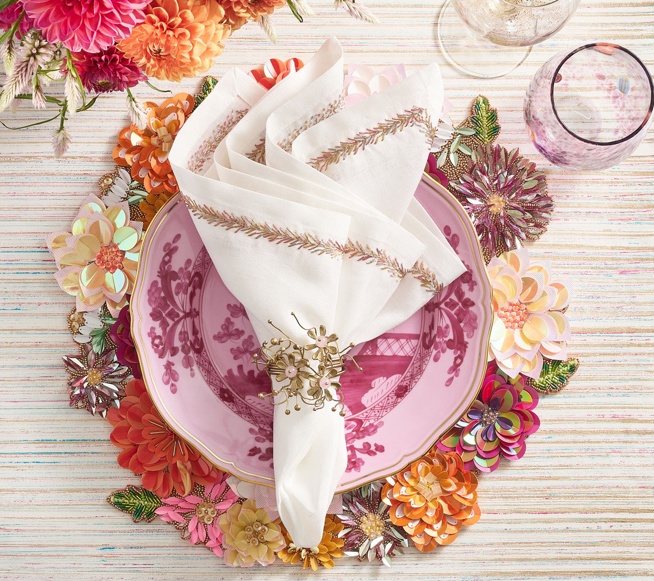 Place setting with a floral placemat, pink plate, white napkin and a blush & gold Flora Napkin Ring 