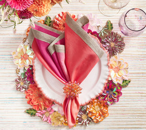 Colorful, beaded Dahlia Placemat with florals of pink, orange, and amethyst beneath a plate with an orange border and a bright pink napkin