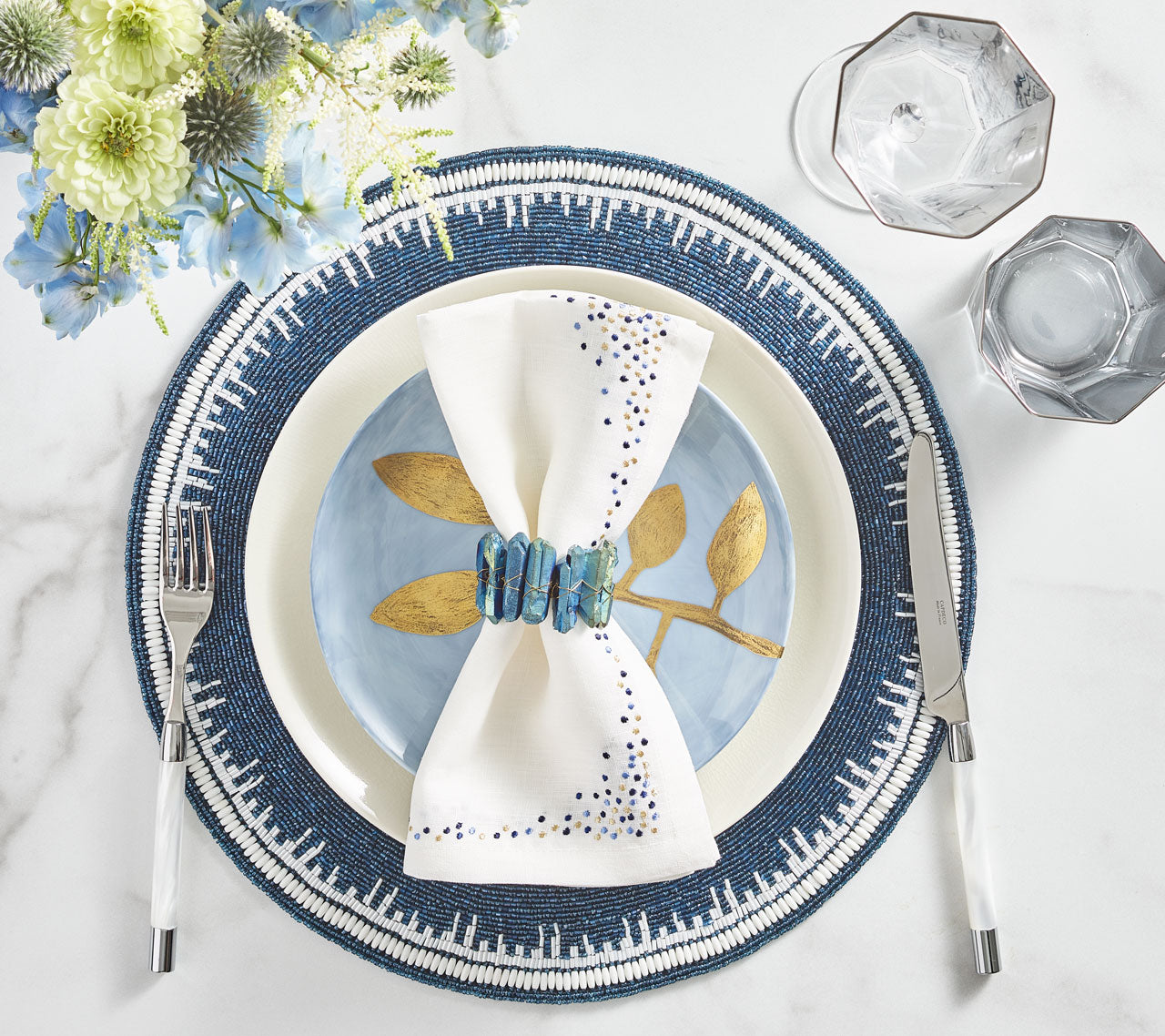 Place setting with a blue beaded placemat, blue plate and a white Pin Dot Napkin with a navy border