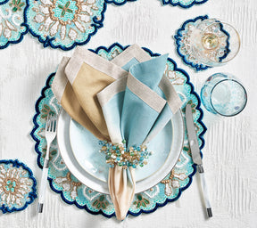 Place setting with a blue, beaded placemat & coasters,  blue & tan napkin held by a natural & seafoam Spritz Napkin Ring 