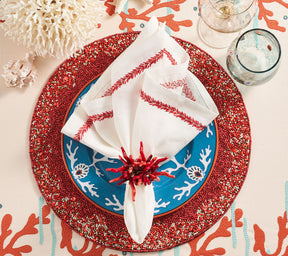 Place setting with a coral & gold beaded Maui Placemat on a table with coral motifs like plates, napkin rings and tablecloth