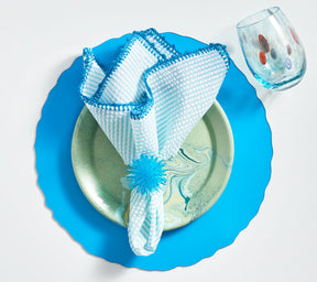 Bright blue placemat underneath a seafoam-striped Seersucker Napkin held by a blue crystal napkin ring