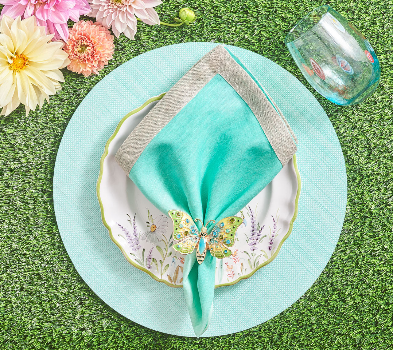 Place setting with florals and a aqua placemat, stemless glass, napkin and a butterfly Arbor Napkin Ring in blue & green 