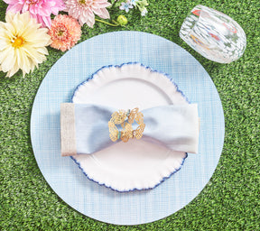 Place setting with a periwinkle Portofino Placemat, white plate with blue trim, and a blue napkin held by a gold butterfly napkin ring