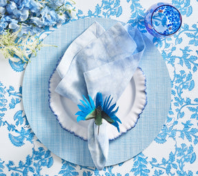 Periwinkle Cloud Napkin held by a bird napkin ring on top of a blue & white plate and blue placemat