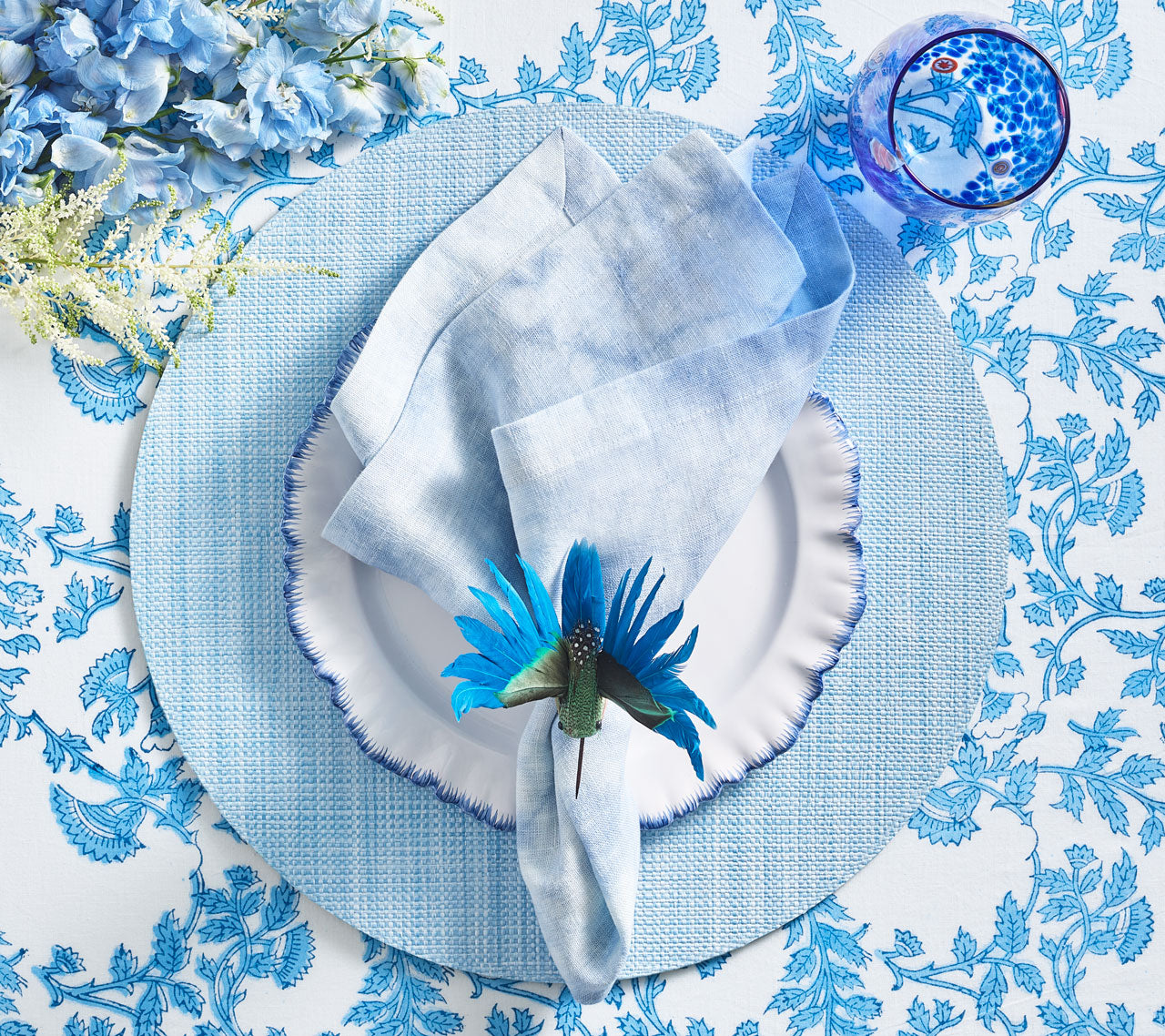 Blue place setting with a periwinkle Portofino Placemat, white plate with blue trim, blue napkin and blue stemless glass