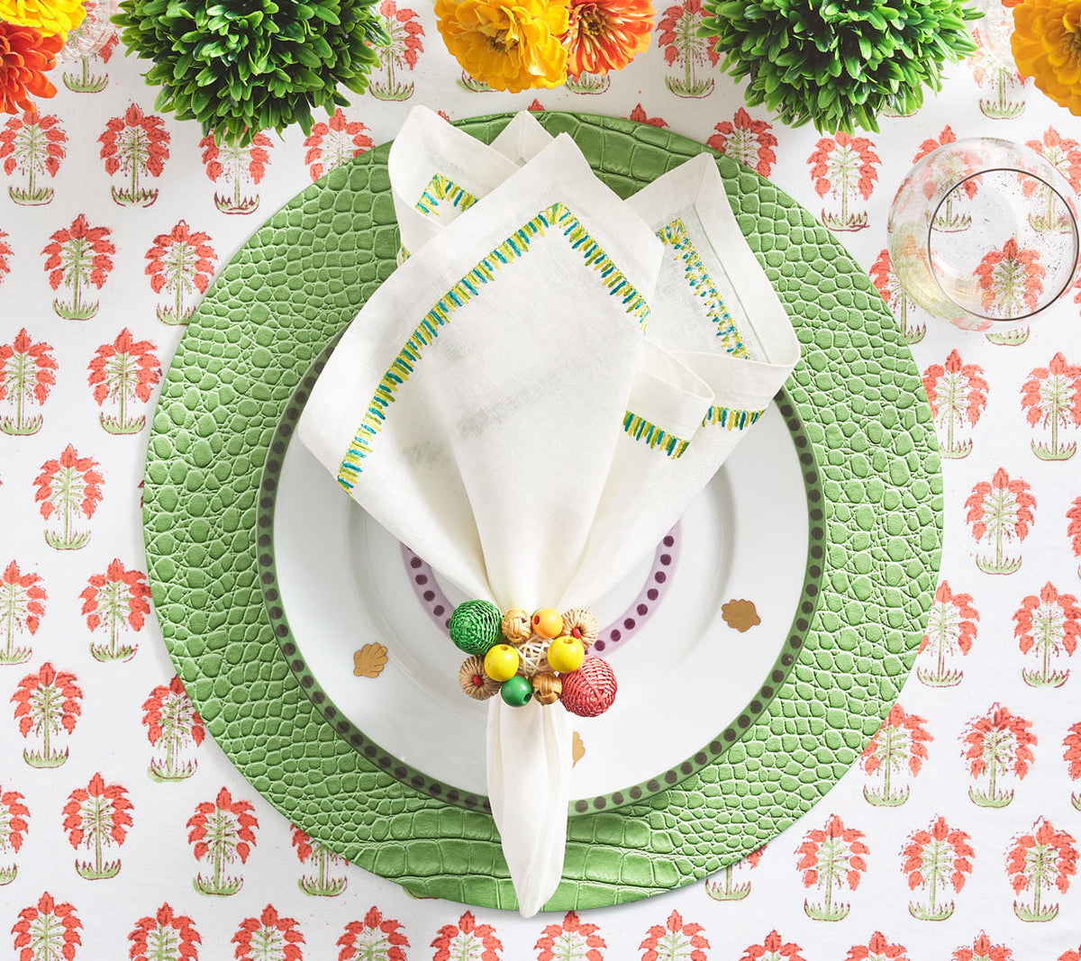 Round, green Croco Placemat  beneath a white napkin with green border on top of a white tablecloth with orange motifs