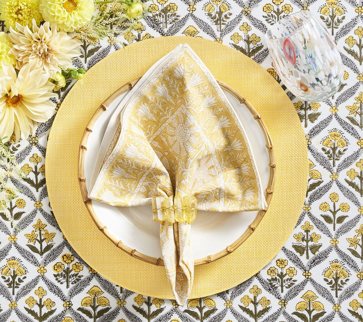Kim Seybert Luxury Provence Napkin in yellow on a yellow place setting and patterned table cloth
