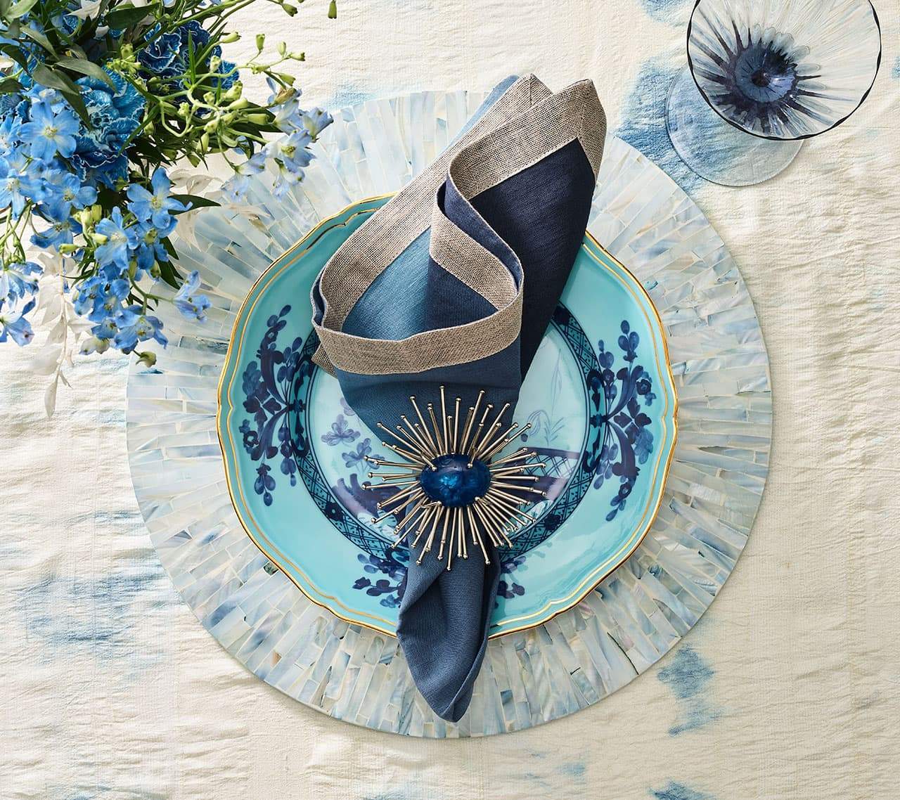Tahiti Placemat in periwinkle underneath an aqua plate, navy napkin, a blue wine glass