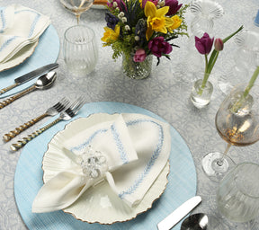 Place setting featuring a periwinkle Portofino Placemat, white plate with gold trim, and a white napkin held by a translucent napkin ring