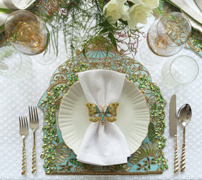 A green and light blue place setting with a beaded placemat, white napkin held by an ornate Arbor Napkin Ring in blue & green 
