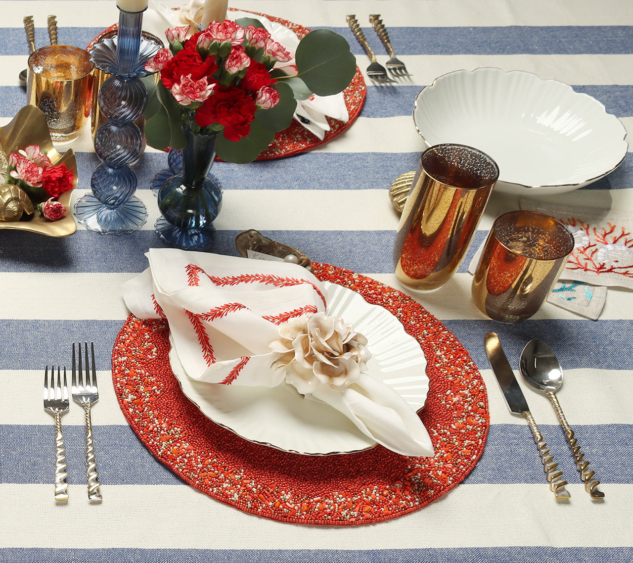 Table with a blue-striped tablecloth red placemat and two blue, glass Tess Bud Vases