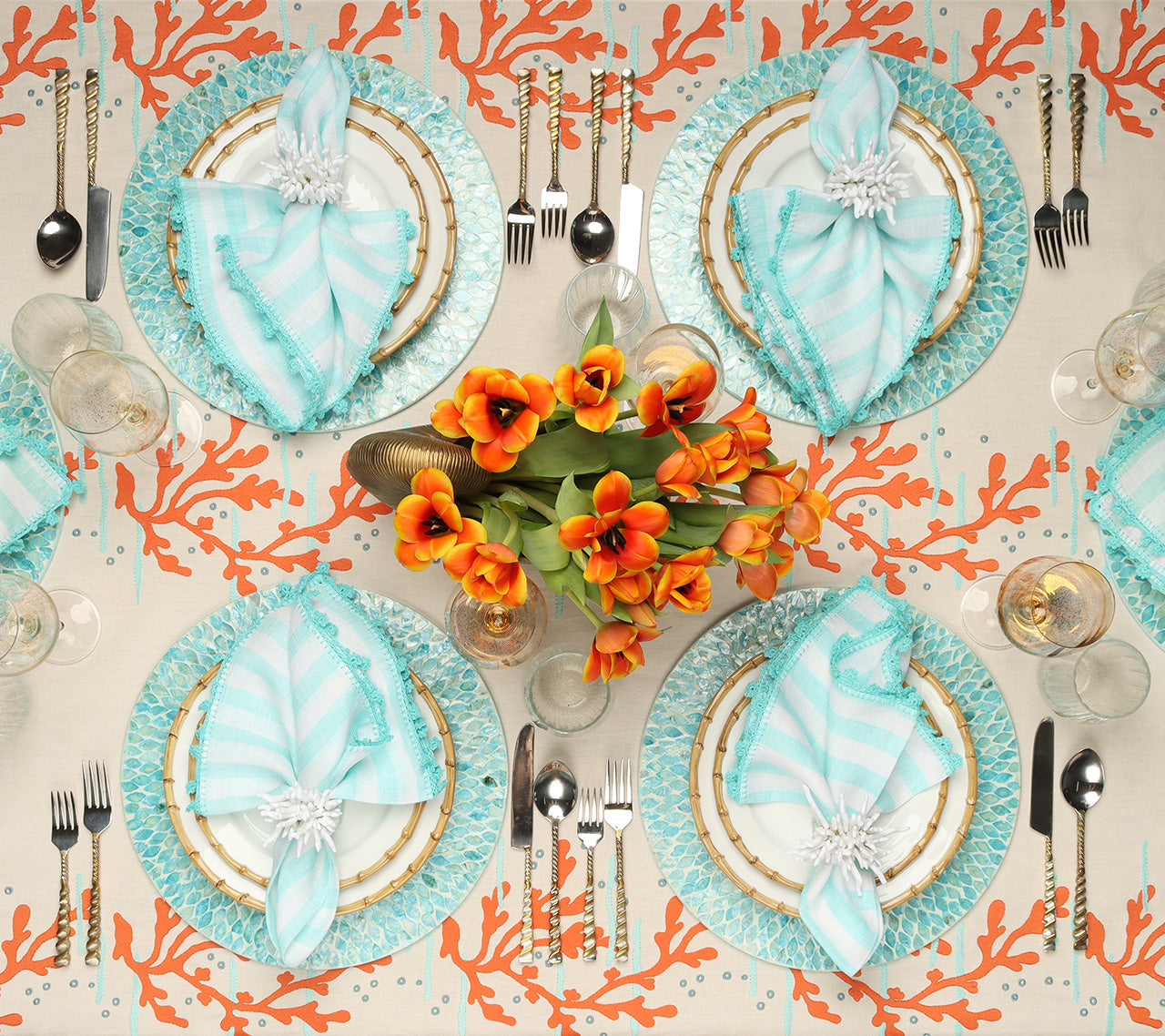 Overhead view of a table with a tablecloth with an orange coral motif, orange floral centerpiece and place settings with seafoam Marquis Placemats