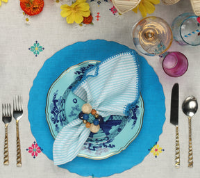 Place setting with a blue placemat underneath a blue plate and seafoam-striped Seersucker Napkin 
