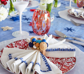 Close up of a Kim Seybert Luxury Filament Napkin in white & navy on a red and white place setting