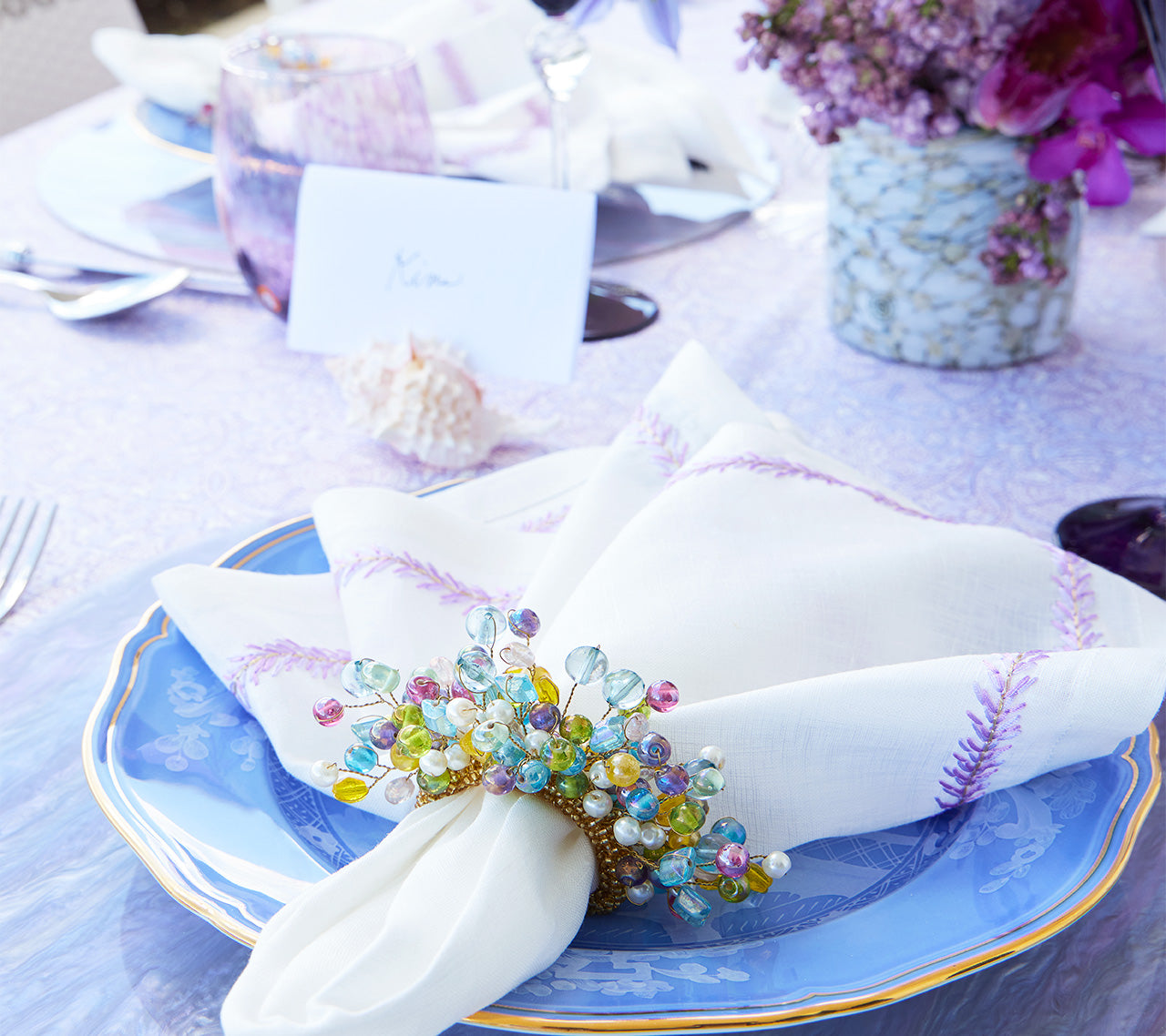 Close up of a blue plate and a napkin held by a multi-pastel colored, beaded Spritz Napkin Ring 